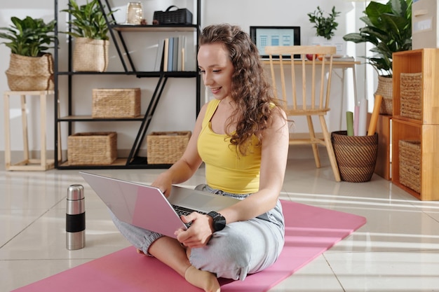 Jonge glimlachende vrouw die aan laptop thuis werkt na ochtendtraining