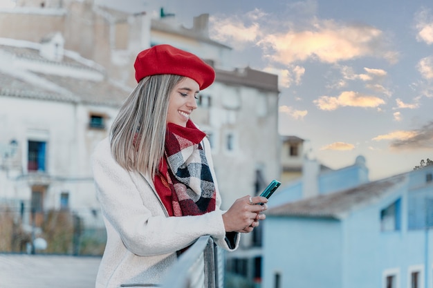 Jonge glimlachende vrouw die een sms-bericht schrijft met haar mobiele telefoon tijdens zonsondergang.