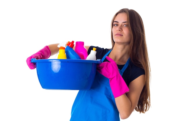 Jonge glimlachende vrouw die met handschoenen schoonmaakdingen in waskom op witte achtergrond in studio houdt