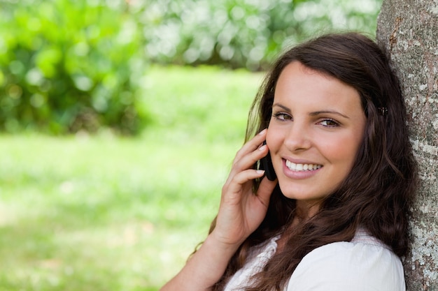 Jonge glimlachende vrouw die op de telefoon spreekt terwijl het bekijken de camera