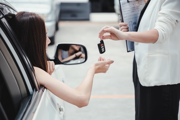 Jonge glimlachende vrouw die sleutel van een nieuwe auto krijgt.