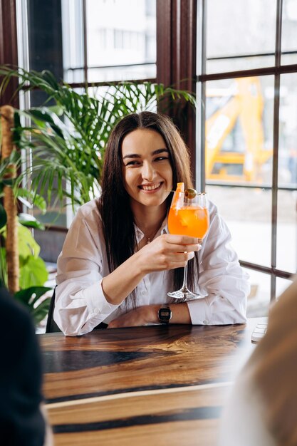 Jonge glimlachende vrouw geniet van een cocktail in een bar-restaurant tijdens rust met vrienden Viering en feestconcept