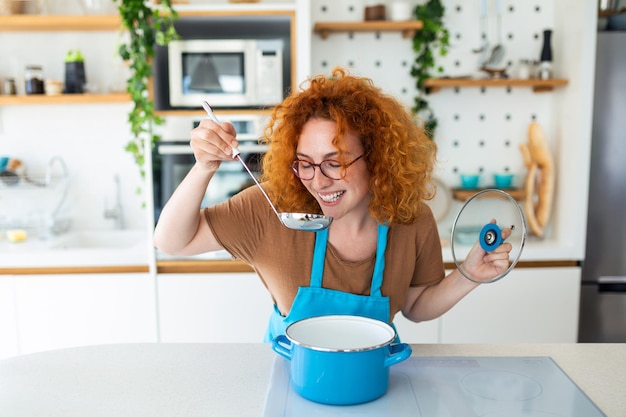 Jonge glimlachende vrouw geniet van smaak en geur tijdens het koken van de lunch in de keuken