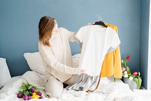 Jonge glimlachende vrouw het organiseren van kleren die op het bed thuis zitten