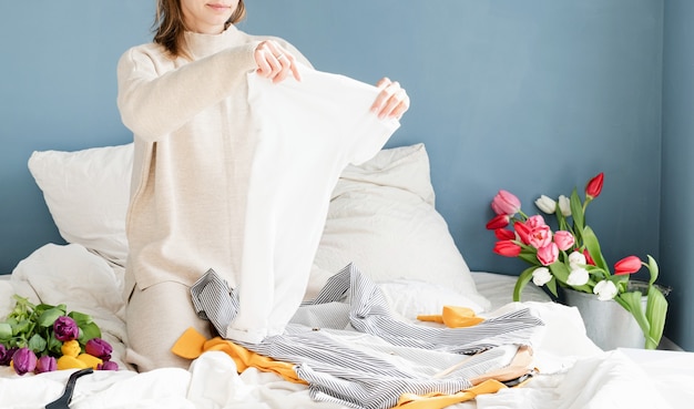 Jonge glimlachende vrouw het organiseren van kleren die op het bed thuis zitten