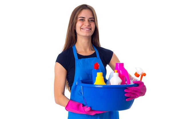 Jonge glimlachende vrouw in blauw T-shirt en schort met handschoenen die schoonmaakspullen in blauwe waskom houden