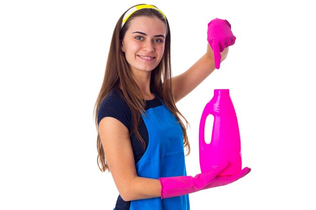 Jonge glimlachende vrouw in blauw T-shirt en schort met roze handschoenen die wasmiddel in studio tonen