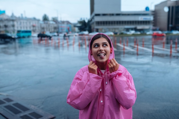 Jonge glimlachende vrouw in een roze regenjas die geniet van een regenachtige dag