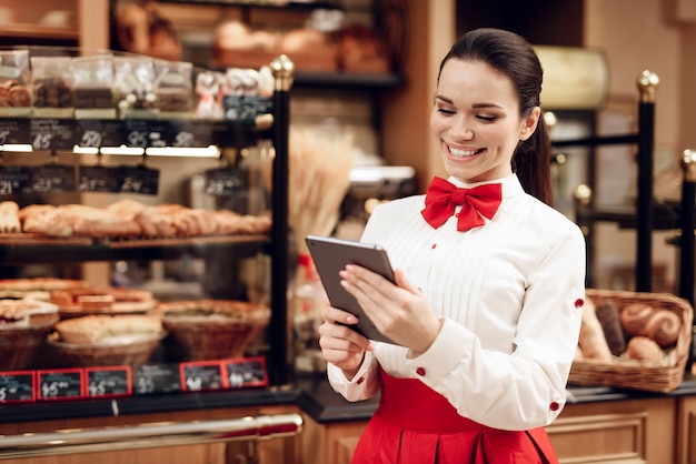 Jonge glimlachende vrouw met behulp van Tablet in moderne bakkerij