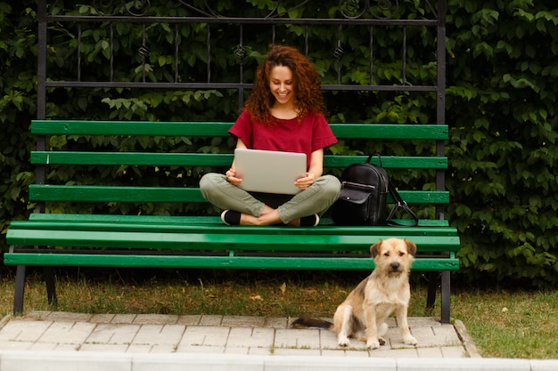 Jonge glimlachende vrouw met haar laptop in het park