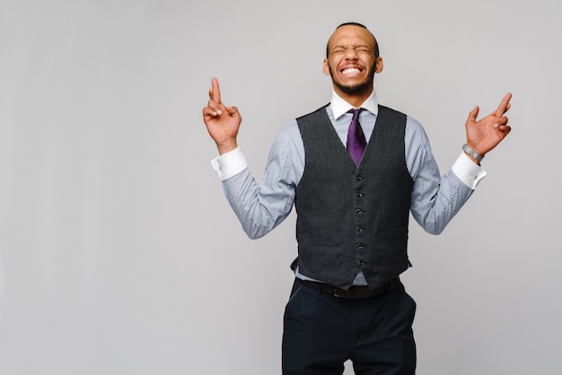 Jonge grappige Afro-Amerikaanse zakenman die vingers kruist, die, op het beste hopen, wonder over grijs wenst.