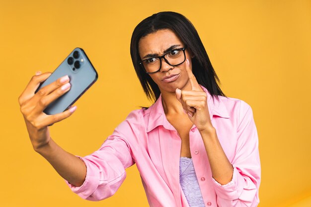 Jonge grappige Afro-Amerikaanse zwarte casual vrouw grimassen en selfie maken op smartphone geïsoleerd op gele achtergrond