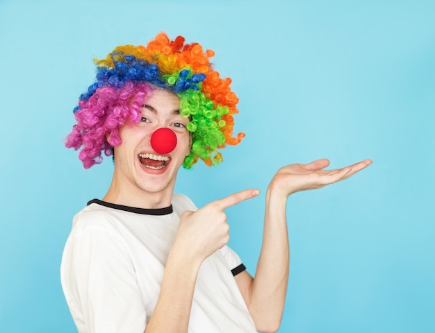 Jonge grappige mannelijke tiener in wit t-shirt op blauw in clown pruik