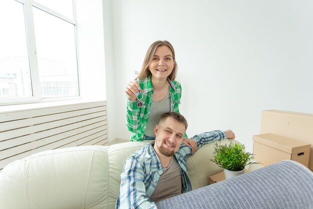 Jonge grappige positieve paar sleutels houden tot een nieuw appartement terwijl ze in hun woonkamer staan. housewarming en gezinshypotheekconcept.