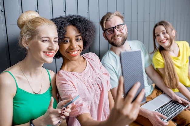 Jonge groep mensen die plezier hebben met smartphones die binnen samen op de muurachtergrond zitten