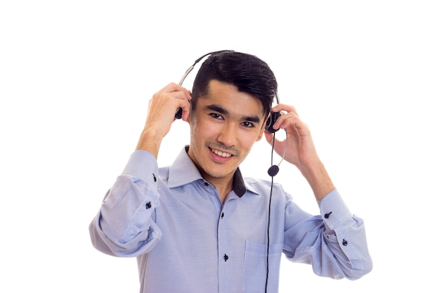 Jonge hansome man met donker haar in blauw shirt met zwarte koptelefoon op witte achtergrond in studio