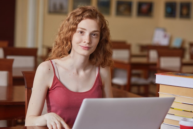 Jonge hardwerkende student direct op zoek, zittend aan een bureau op de campus, studeren met behulp van laptop