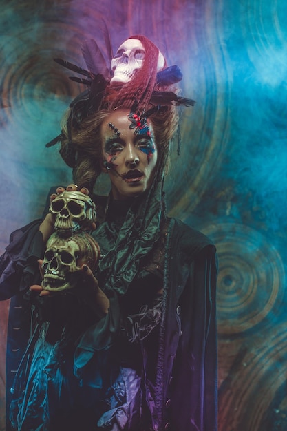 Foto jonge heks die schedel houdt heldere make-up en rook halloween-thema studio-opname