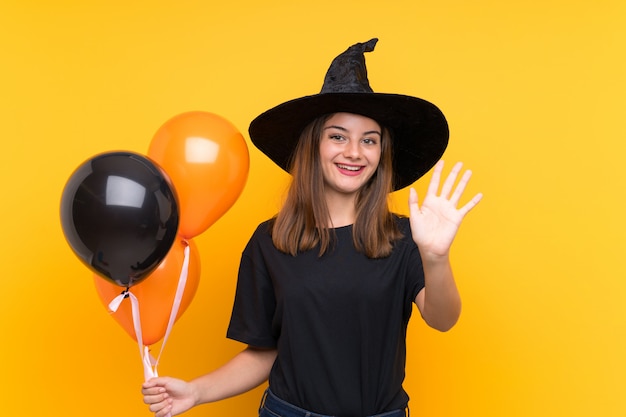 Jonge heks die zwarte en oranje luchtballons voor Halloween-partijen houden die met hand met gelukkige uitdrukking groeten