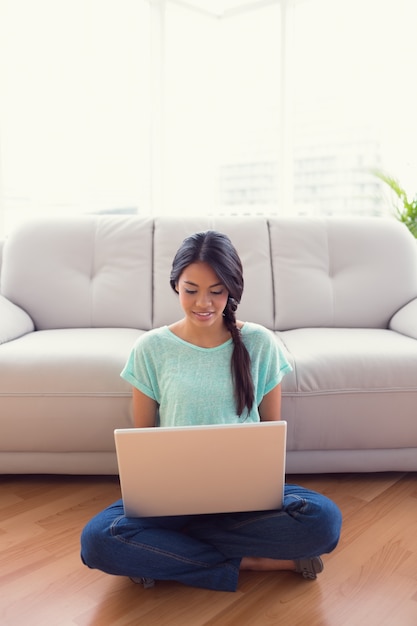 Jonge het glimlachen meisjeszitting op vloer die haar laptop met behulp van