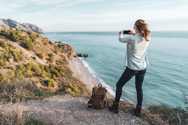 Jonge heupvrouw met een rugzak die en de kust op een mooie dag onderzoekt fotografeert. Concept van exploratie en avonturen