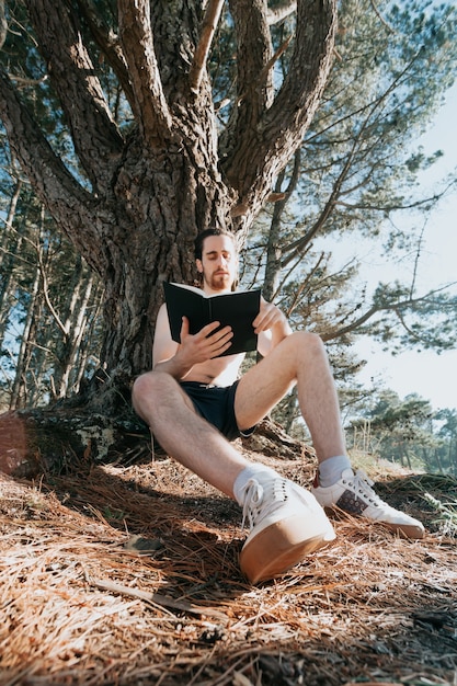 Jonge hippieman die een boek leest, groothoekopname, sociaal netwerk, zomerse sfeer ontspannen levensstijl