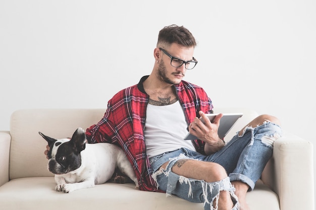 Jonge hipster kijkt naar zijn tablet naast zijn hond die op de bank zit