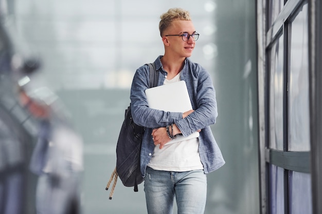 Jonge hipster man in mooie kleding staat binnen en in de buurt van auto