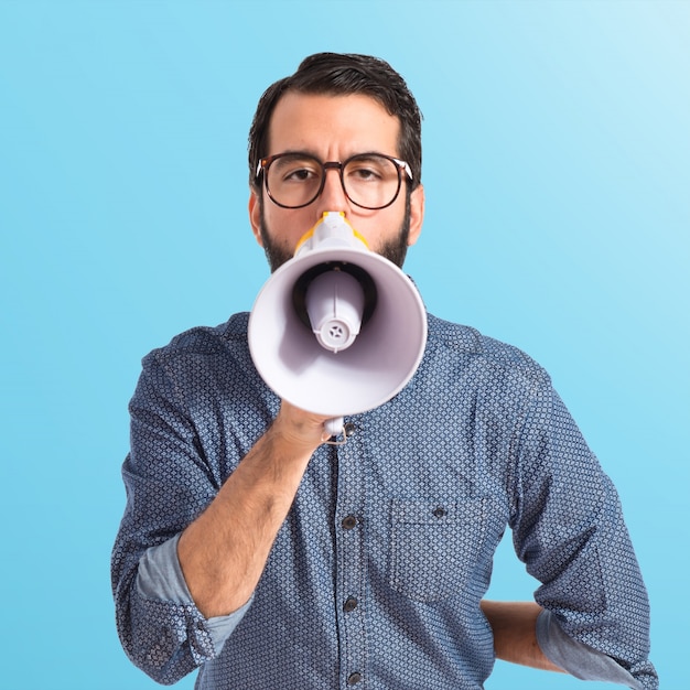 Jonge hipster man schreeuwen door megafoon op kleurrijke achtergrond