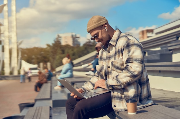 Jonge hipster man zit buiten met koffie tijdens het controleren van e-mail werken bloggen online studeren