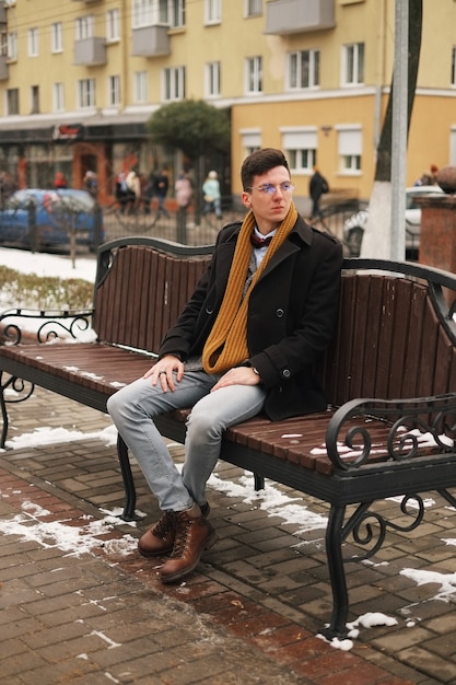 Jonge hipster man zit op een bankje, kijkt weg, in de winter buiten