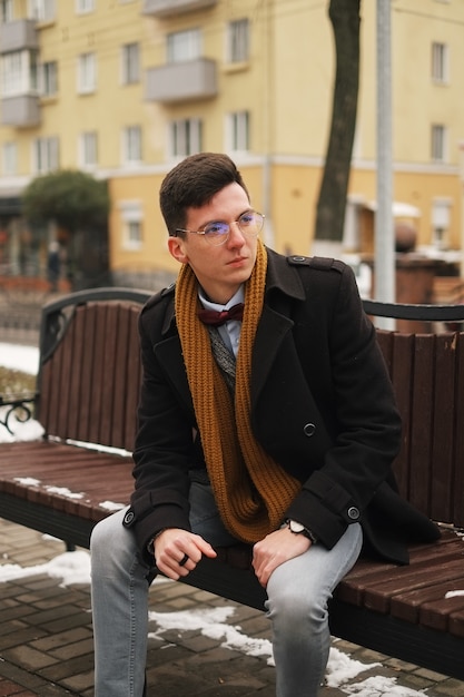 Jonge hipster man zit op een bankje, kijkt weg, in de winter buiten