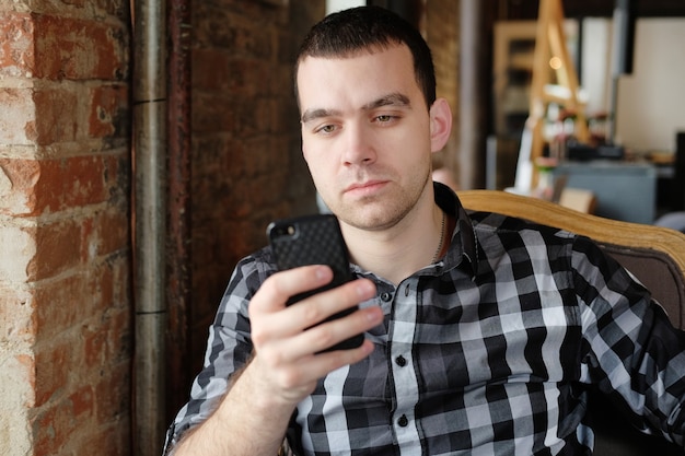 Jonge hipster met een smartphone. beambte op lunch praten aan de telefoon. een succesvolle jongeman in een donker geruit overhemd in het café doet zaken. zakelijke bijeenkomst.