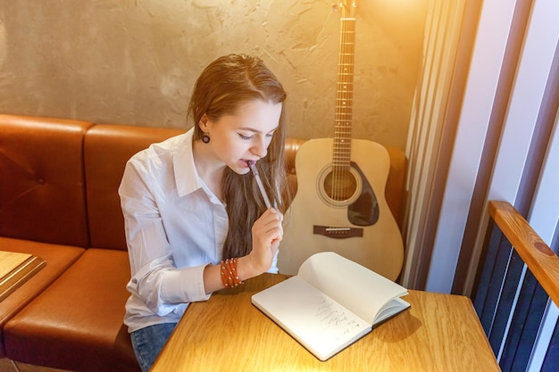 Jonge hipster vrouw aan tafel zitten en gitaar spelen in café achtergrond tienermeisje leren pla