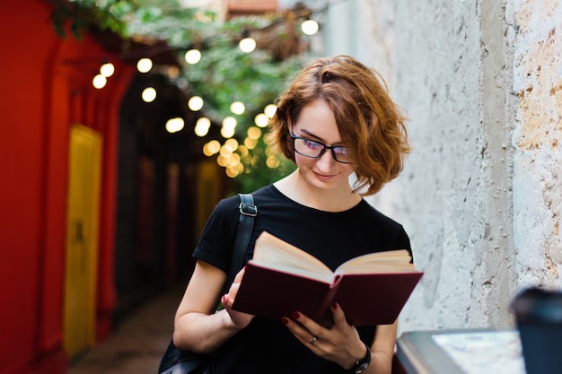 Jonge hipster vrouw in glazen met korte kapsels leesboek in straat café