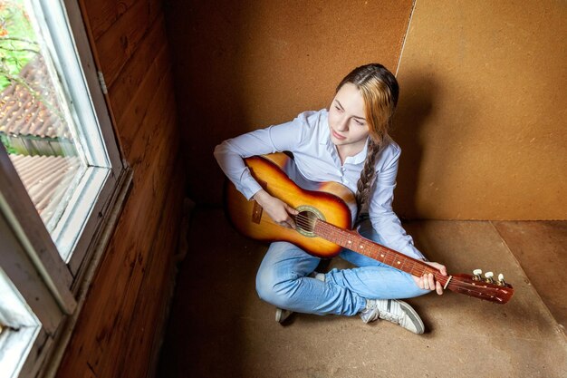 Jonge hipster vrouw zittend op de vloer en gitaar spelen thuis Tiener meisje leren om liedjes te spelen en muziek te schrijven in haar kamer Hobby levensstijl ontspannen Instrument vrijetijdsbesteding onderwijs concept