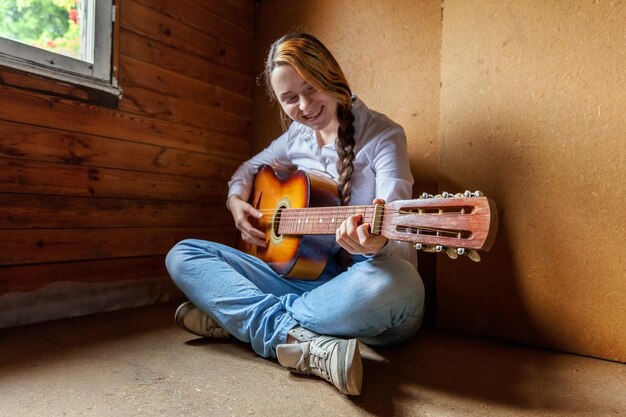 Jonge hipster vrouw zittend op de vloer en gitaar spelen thuis Tiener meisje leren om liedjes te spelen en muziek te schrijven in haar kamer Hobby levensstijl ontspannen Instrument vrijetijdsbesteding onderwijs concept