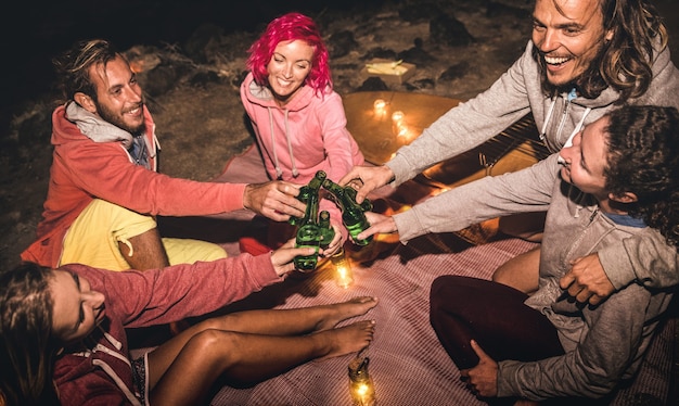 Jonge hipstervrienden die samen plezier hebben 's nachts strandfeest met kampvuurlicht - vriendschapsreisconcept met jonge mensenreiziger die bier drinkt op zomersurfcamping - hoge iso-afbeelding