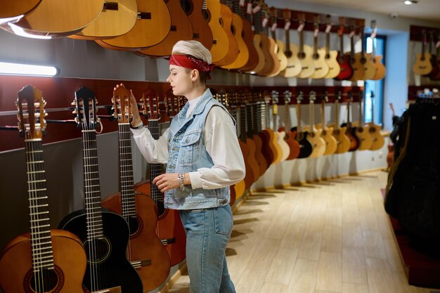 Jonge hipstervrouw die akoestische gitaar in instrumentenwinkel kiezen. Vrouwelijke koper bij muziekwinkel
