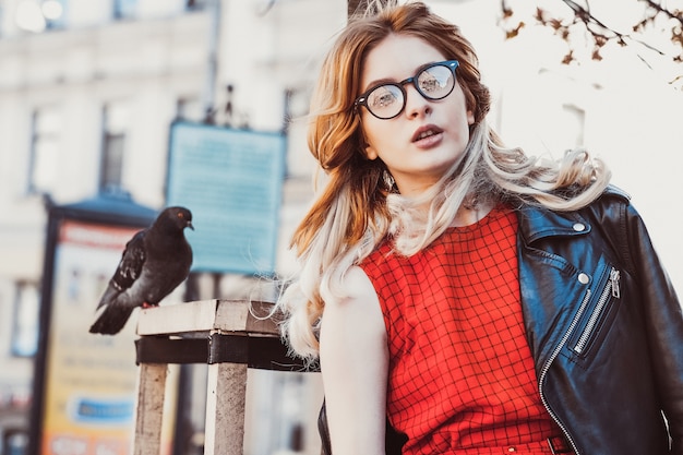 Jonge hipstervrouw die rode kleding in de stad draagt. Lente en vogels duiven.