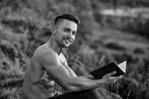 Jonge homo. Glimlachende gespierde man met boek buiten