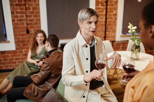 Jonge homo man in witte vrijetijdskleding met glas rode wijn en praten met Afro-Amerikaanse meisje staf