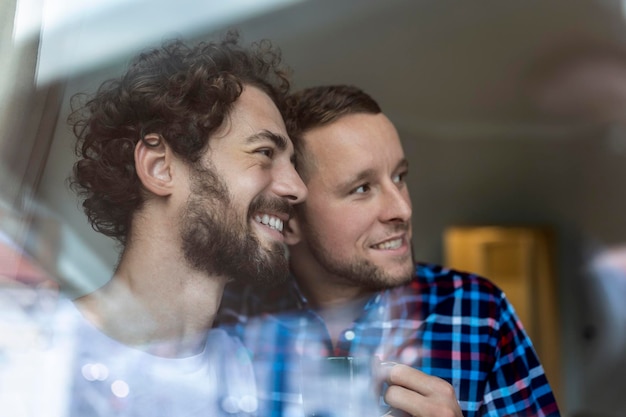 Jonge homo paar verliefd kijkt uit het raam Twee jonge androgyne mannen glimlachen samen en hebben koffie