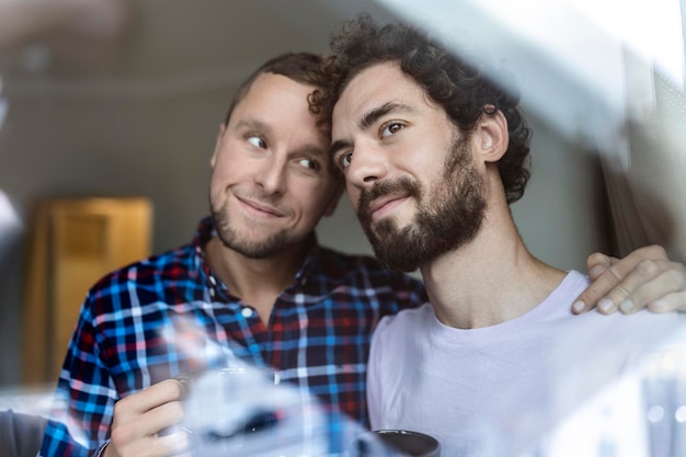 Foto jonge homo paar verliefd kijkt uit het raam twee jonge androgyne mannen glimlachen samen en hebben koffie