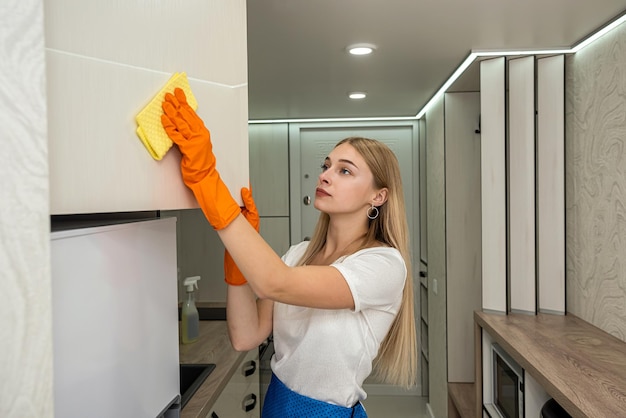 Jonge huisvrouw die de keuken schoonmaakt met rubber en speciale spray