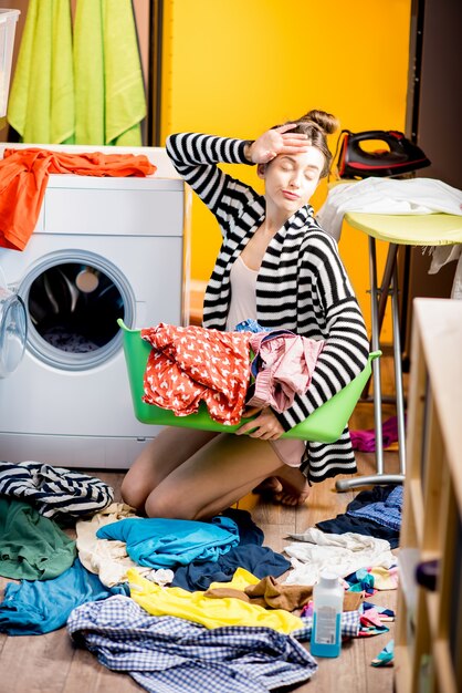 Jonge huisvrouw die een mand met kleren vasthoudt in de buurt van de wasmachine die thuis op de vloer zit