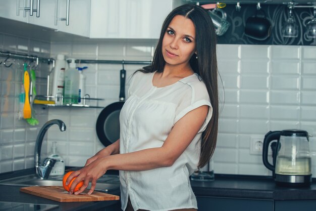 Jonge huisvrouw in de keuken om de sinaasappel op het bord te snijden