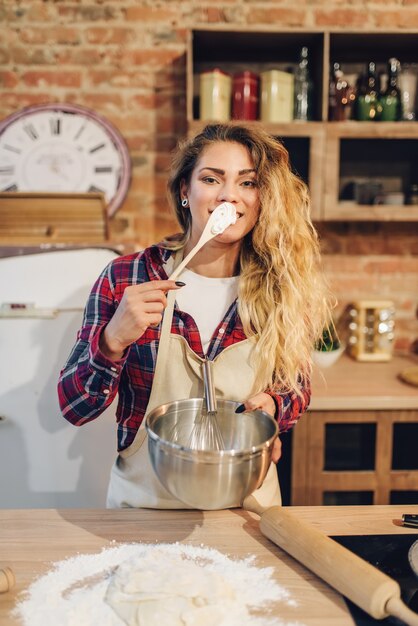 Jonge huisvrouw in een schort smaakt vers deeg