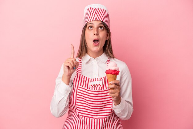 Jonge ijs maker vrouw met ijs geïsoleerd op roze achtergrond omhoog wijzend met geopende mond.