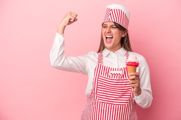 Jonge ijsmachine vrouw met ijs geïsoleerd op roze achtergrond die vuist opheft na een overwinning, winnaar concept.